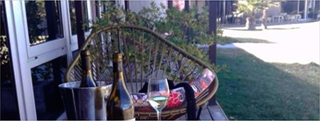 Imagen de un sillón y una mesita con copas y vinos en un exteior.